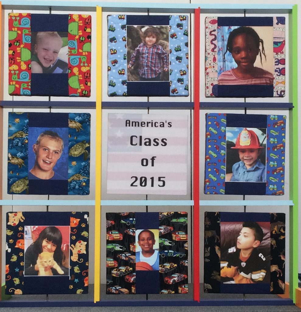 Nine large 12 inch squares are contained in a wooden frame that is painted with primary colors. Each two-sided square spins independently on a vertical axis. On the front side, eight large up-close photos of children of various skin tones surround a center square that reads “America’s Class of 2015. When the eight perimeter squares are turned around, the back side reads: “Mercy / Killing / Mean/ Disabled / People / Killed / By Those / They Love.” The back center square reads: “In 2015 in the United States 28 disabled children and 27 disabled adults were killed by their families.”