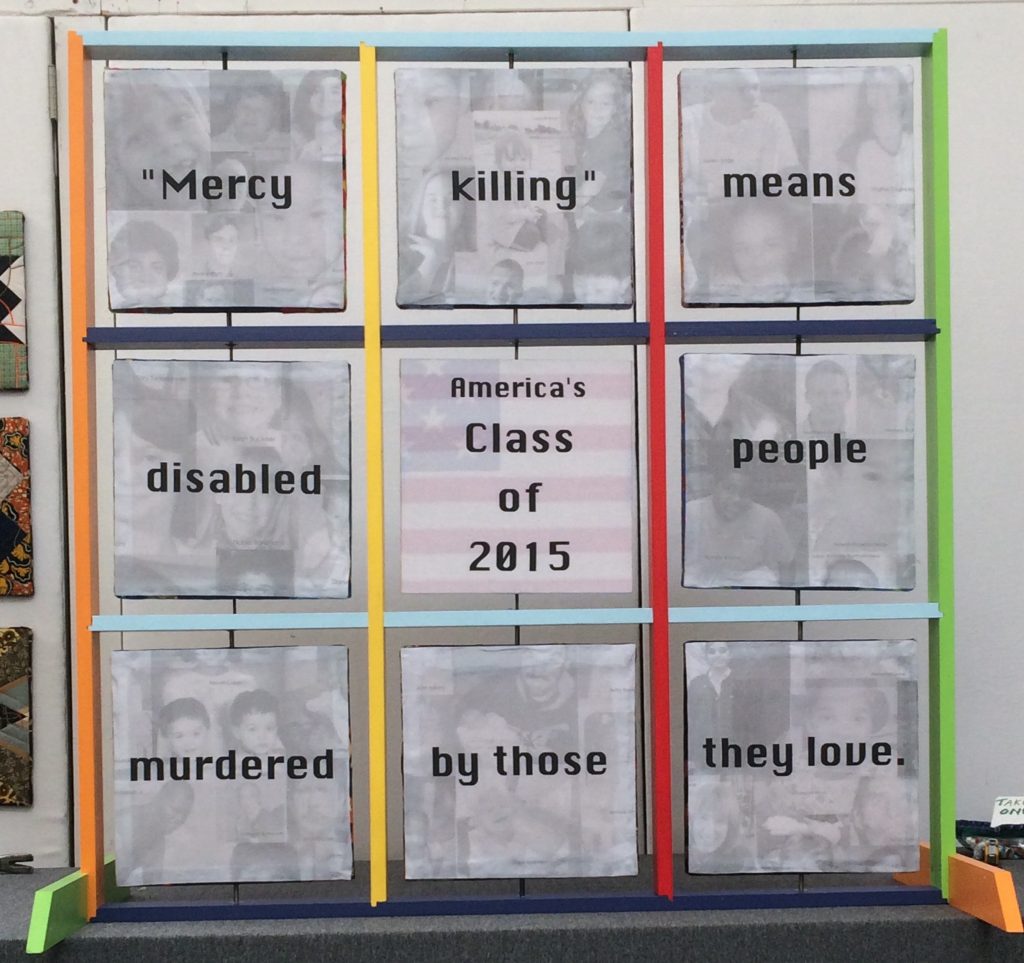 Nine large 12 inch squares are contained in a wooden frame that is painted with primary colors. Each two-sided square spins independently on a vertical axis. On the front side, eight large up-close photos of children of various skin tones surround a center square that reads “America’s Class of 2015. When the eight perimeter squares are turned around, the back side reads: “Mercy / Killing / Mean/ Disabled / People / Killed / By Those / They Love.” The back center square reads: “In 2015 in the United States 28 disabled children and 27 disabled adults were killed by their families.”