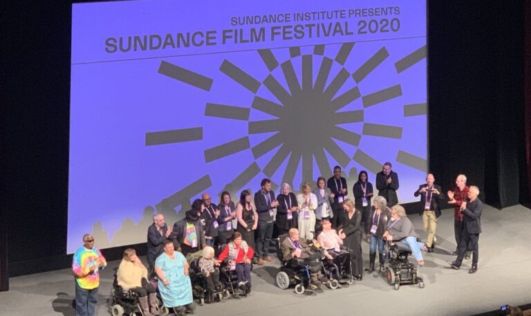 A group of people on stage with "Sundance Festival" on the screen behind them.
