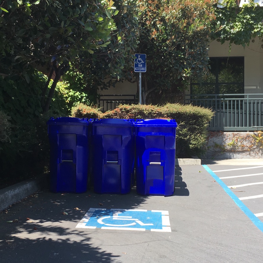 Three recycling bins take up the van accessible parking space.