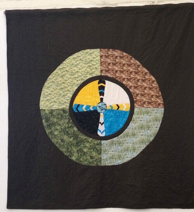 Fabric piece - black background with a circle made from gray, brown, blue and orange fabric.